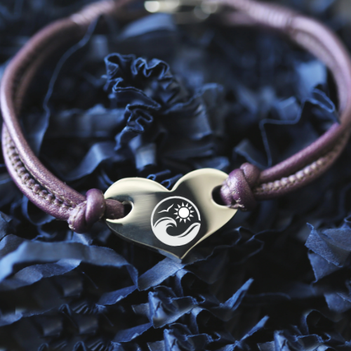 Bracelet with a heart-shaped clasp featuring a sun and wave design on a blue textured background.